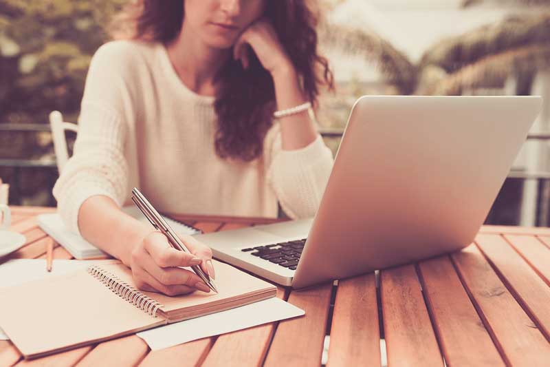 Woman writing while using a laptop